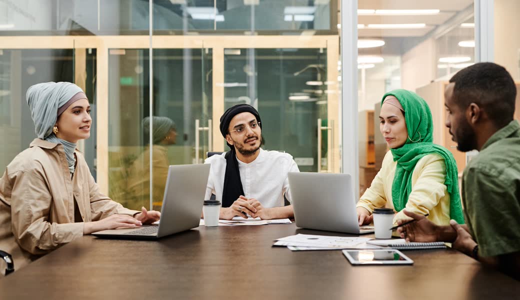Four colleagues with laptops talking around a meeting-room table